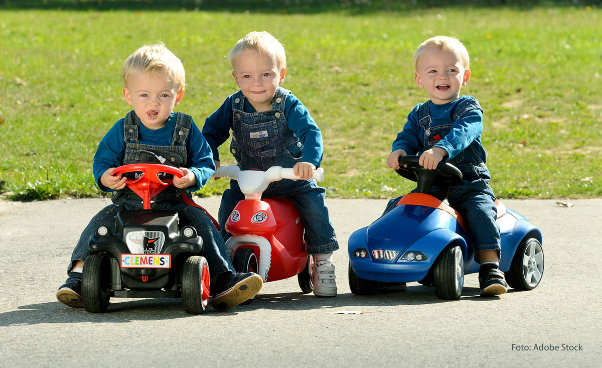 Drei Kinder auf einem Bobby-Car, Foto: Adobe Stock