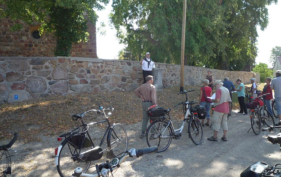 Foto: Fahrradgruppe mit Karten in der Hand vor einem Friedhofsmauer