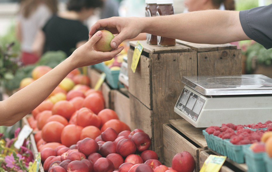 Foto: Eine Hand übergibt einen Apfel in die Kundenhand über den Marktstand hinweg.