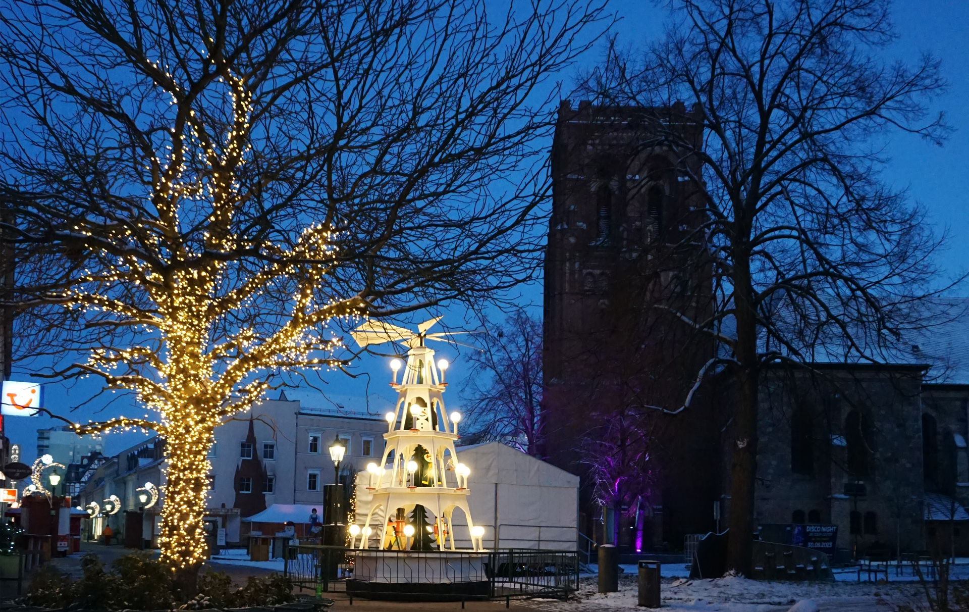 Foto: leuchtende Pyramide und weihnachtlich geschmückte Straße im Abendlicht