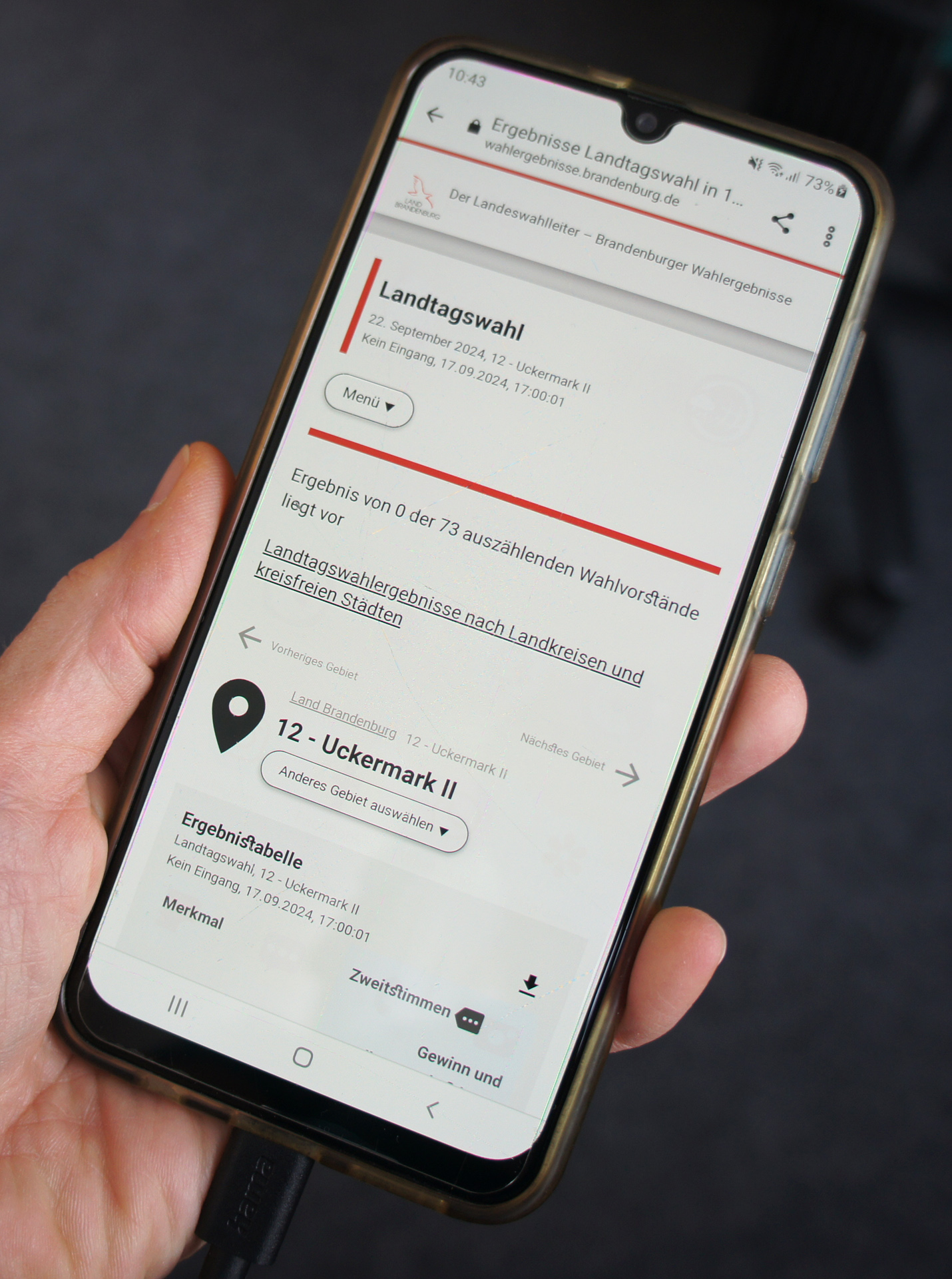 Foto: Hand mit Smartphone, auf dem das Wahlportal angezeigt wird.