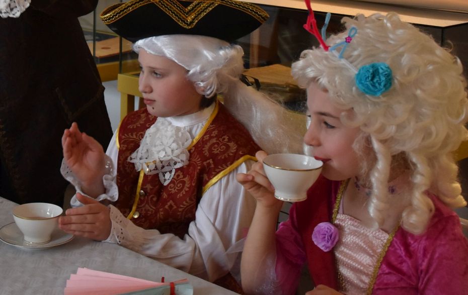 ein Mädchen und ein Junge tragen historische Kostüme und trinken Tee