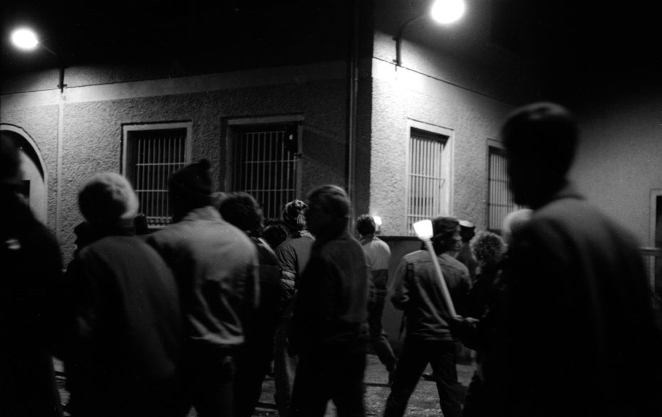 Menschen laufen im Dunkeln am Stasi-Gebäude vorbei.
