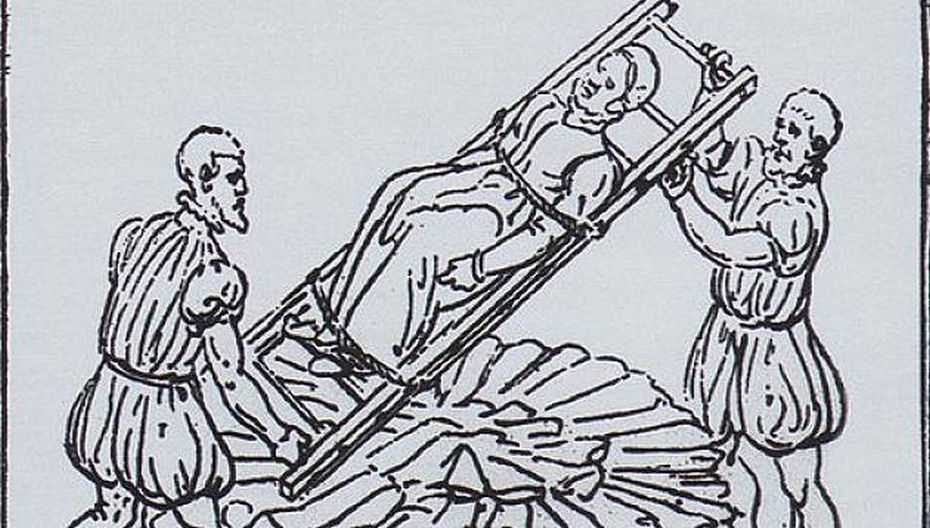 Zwei Männer heben eine auf eine Leiter gebundene Hexe auf den Scheiterhaufen