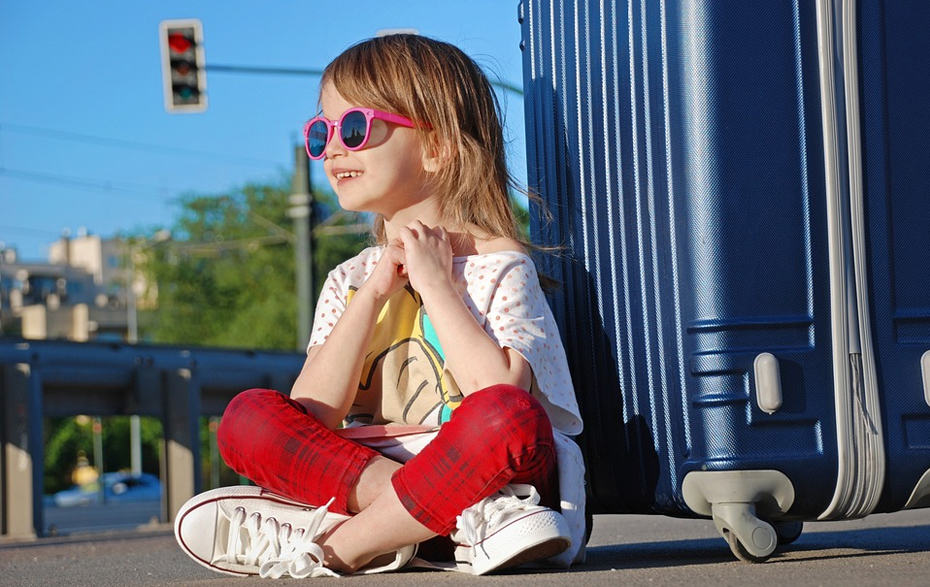 Foto: Mädchen mit Sonnenbrille lehnt an einem Rollkoffer