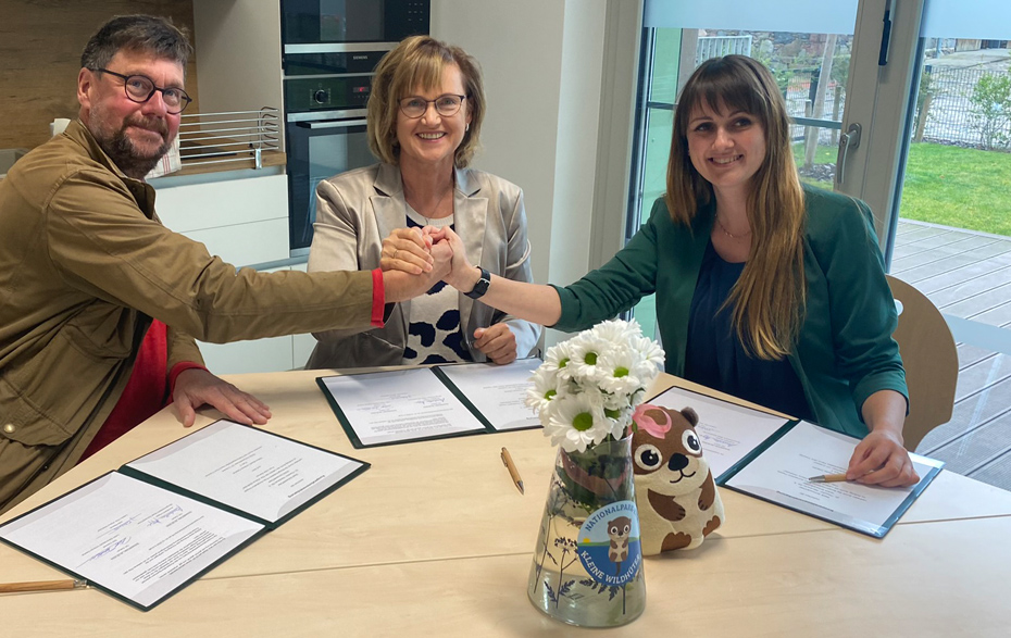 Foto: 3 Personen am Tisch reichen sich die Hände