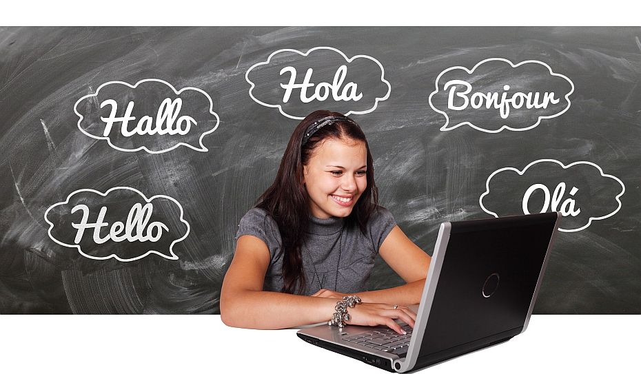 Ein Mädchen sitzt vor einem Laptop. Um sie herum ist das Wort Hallo in unterschriedlichen Sprachen.