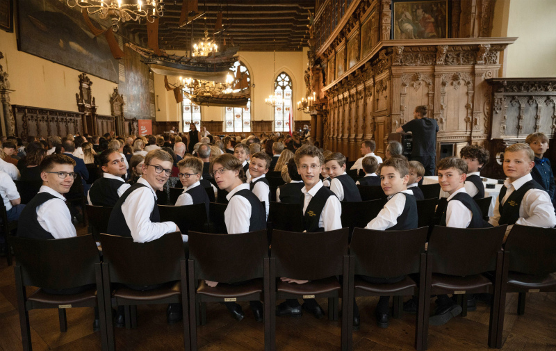 Foto: festlich gekleidete Knaben in einem Saal drehen sich nach hinten um und blicken in die Kamera