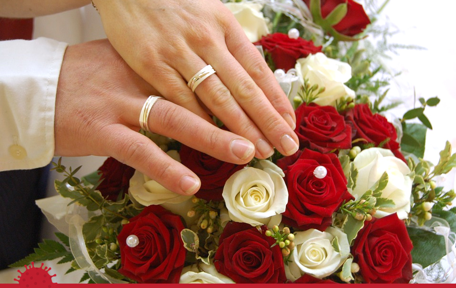 Foto: zwei Hände mit Eheringen über einem Rosenstrauß